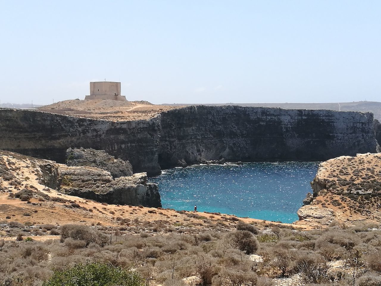 water, built structure, architecture, blue, tranquility, tranquil scene, clear sky, scenics, nature, beauty in nature, day, outdoors, non-urban scene, rock formation, sky, geology, no people, remote, cliff, natural landmark, sea, tourism, shore