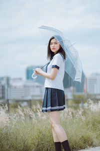 Portrait of young woman with umbrella standing by plants on field