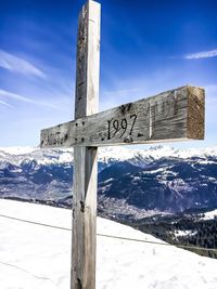 Wooden cross on snow covered landscape against sky