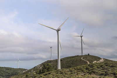 Roads leading towards windmills against cloudy sky