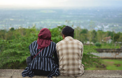 Rear view of couple sitting on rock looking at view