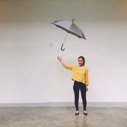 Full length of mid adult woman throwing umbrella while standing against wall