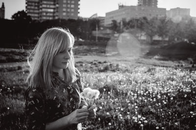 Woman holding dandelion while standing on field