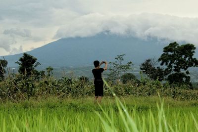 Rear view of man standing on field against sky