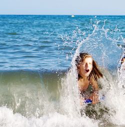 Happy boy splashing water in sea against sky