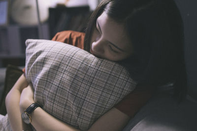 Young woman holding pillow while sitting on bed