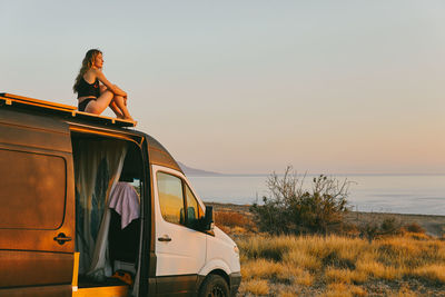 Young woman on camper van looking out to the sunrise in baja, mexico.