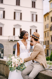 Couple embracing while sitting against building