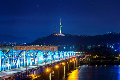 Illuminated bridge over river against sky at night