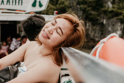 Smiling young woman with eyes closed leaning on railing