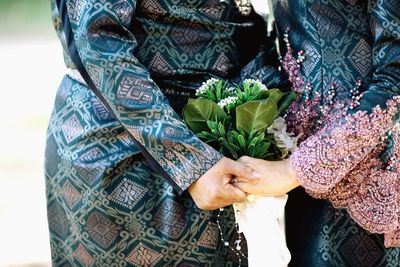 Midsection of couple holding hands and flower bouquet