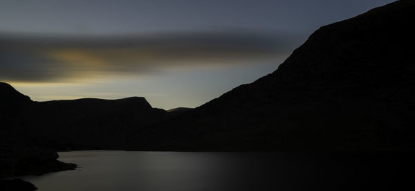 Scenic view of lake and silhouette mountains against sky at sunset