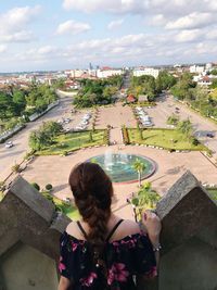 Rear view of young woman looking at view while standing by retaining wall against cloudy sky