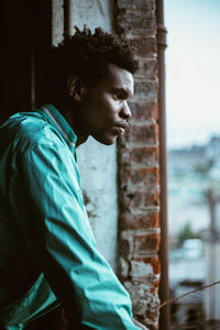 Portrait of young man standing against window