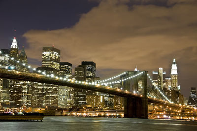 Brooklyn bridge over river against cityscape at night