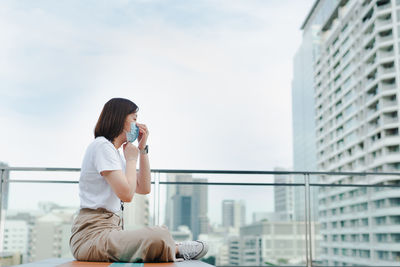 Solo asian woman wear protective mask during outdoor break and relax at rooftop with city background