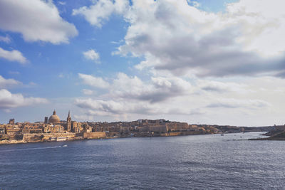 View of buildings by river against cloudy sky