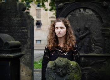 Young woman standing by sculpture at graveyard