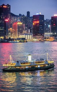 Illuminated ship in sea against city