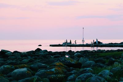 People on jetty by sea during sunset