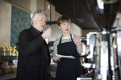 Female barista and owner gesturing while discussing in cafe