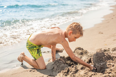 Shirtless boy playing on shore at beach during summer