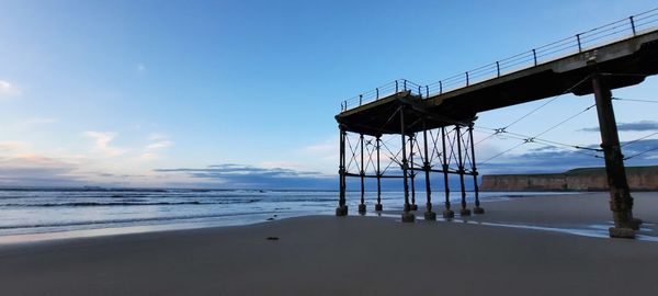 Pier viewed on beach against sky