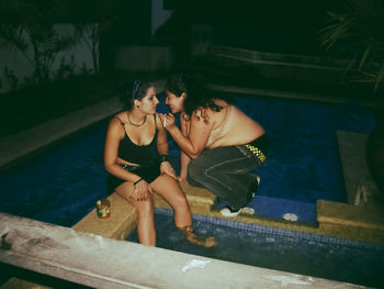 Full length of siblings sitting on swimming pool