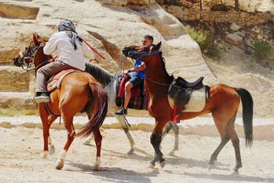 Men riding horses on sand