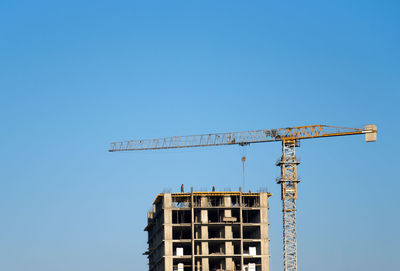 Low angle view of crane against clear blue sky