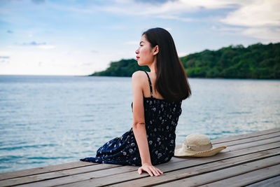 Young woman sitting on pier over sea against sky