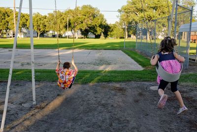 Siblings playing at swing on playground