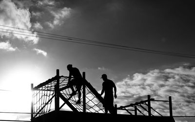 Low angle view of silhouette people standing by railing against sky