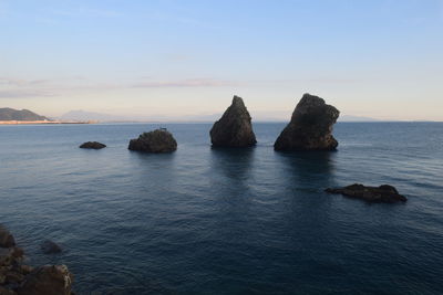 Rocks in sea against sky during sunset