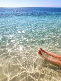 Low section of person on sea shore against sky