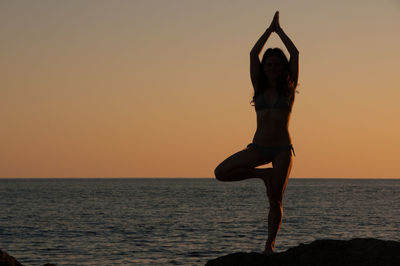 Rear view of woman meditating at beach during sunset