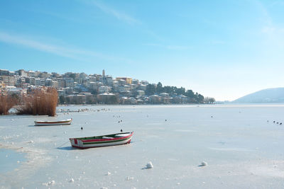 Snowy lake scene with boat trapped in the lake and town of kastoria as background