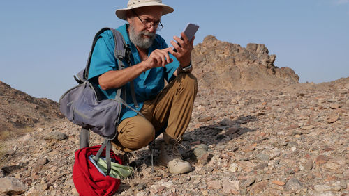 Senior man sitting on rock and using mobile phone 