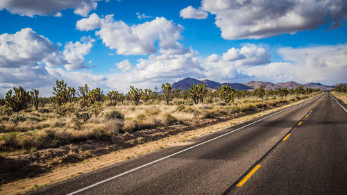 Empty road amidst landscape against cloudy sky