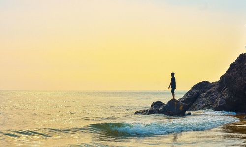 Boy standing on rock at beach during sunset