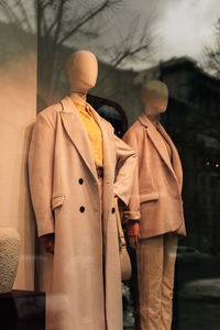 Trendy mannequins in a store window dressed in  fashion cloth. beige long coat and  yellow shirt