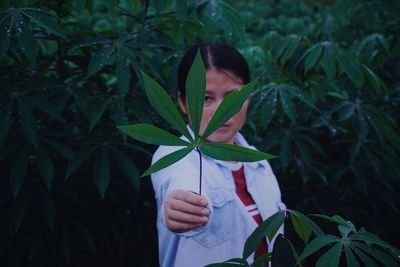 Portrait of woman holding leaves by plant