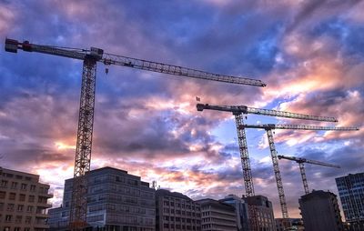 Low angle view of cranes against cloudy sky