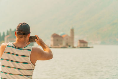 Male taking photo of tourist attraction our lady of the rock in montenegro.