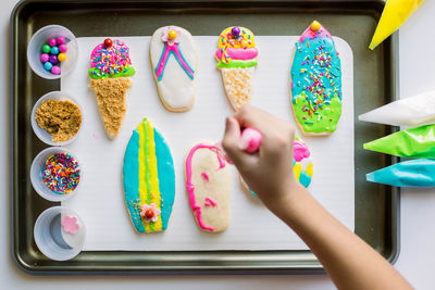 High angle view of various cookies on table and human hand decorating 