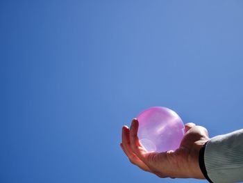 Cropped hand of person holding balloon against clear blue sky