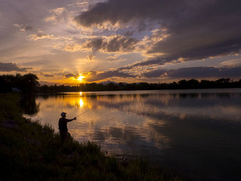 Silhouette man standing by lake against sky during sunset