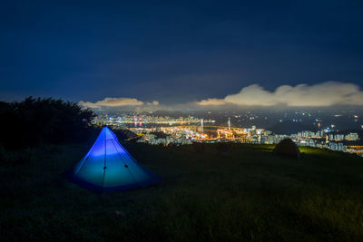 Illuminated city on field against sky at night