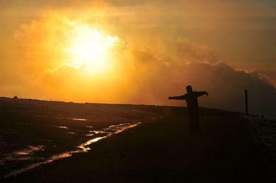 Silhouette man standing on sea against sky during sunset