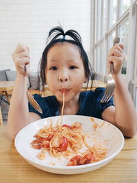 Portrait of girl eating spaghetti while sitting in restaurant